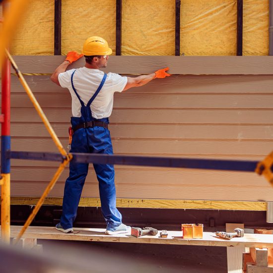 Worker installing vinyl siding panels on residential exterior wall